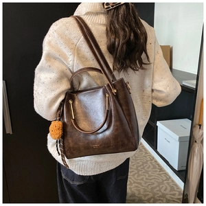 Detail of dark brown faux leather tote with golden metal U-handle and plush charm