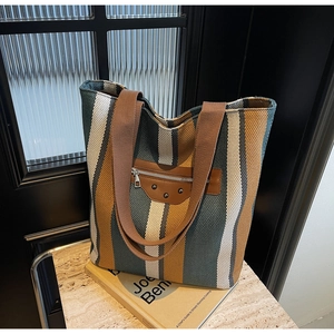 Detail of striped canvas tote bag with brown leather patch and woven shoulder straps