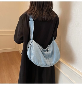 Back view of a model wearing a light blue denim crescent shoulder bag with wide strap