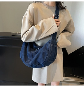 Detail view of large dark blue denim crescent tote bag with adjustable wide canvas strap