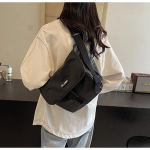 Close-up of black crossbody bag with wide strap on model in cozy interior background