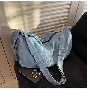 Detail of light blue denim tote bag with adjustable strap on a black striped seat