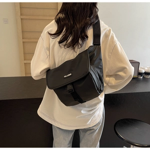 Rear view of a black large-capacity nylon messenger bag worn by a model in a modern room