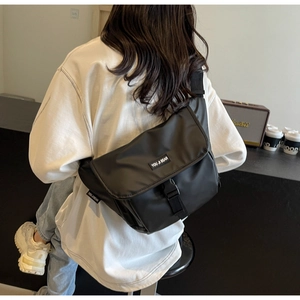 Rear view of a black waterproof messenger bag shown in a modern urban cafe setting