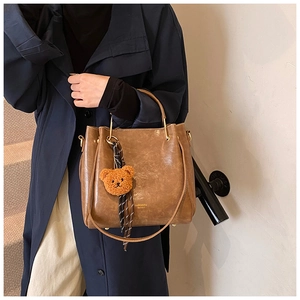 Brown vintage tote bag featuring gold ring handles and a cute plush bear charm accessory