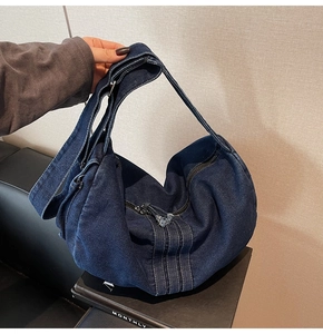 Detail of deep blue denim tote bag featuring wide shoulder strap and metal zipper with tassel