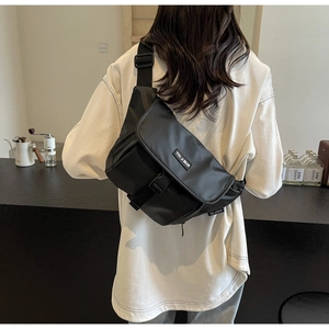 Detailed back view of a black nylon messenger bag worn by a model in a minimalist cafe