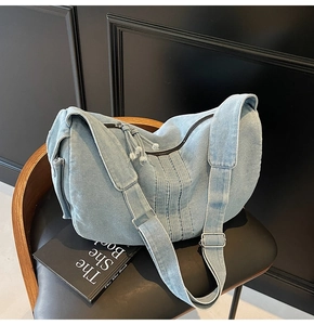 Detail of light blue denim tote bag showing distressed denim tassels and zipper hardware