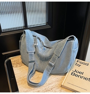 Detail of light blue denim tote bag showing crescent shape and zipper on marble surface