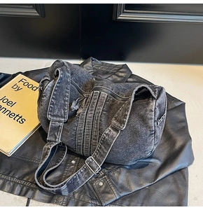 Detail of dark gray washed denim barrel bag featuring adjustable strap and metallic buckles