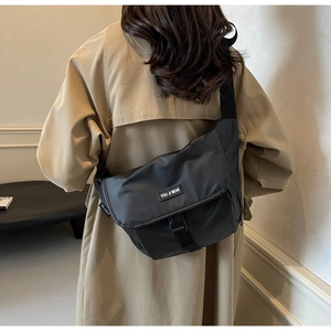 Close-up of black messenger bag with buckle closure worn on a beige trench coat