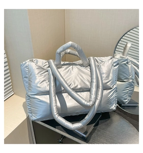 Detail of silver metallic quilted tote bag with padded handle on dark surface