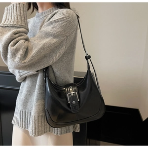 Dettaglio borsa a mezzaluna nera con fibbia argentata indossata su un maglione grigio