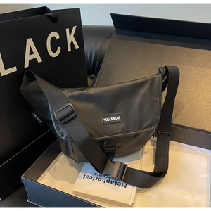 Close-up of black messenger bag with adjustable strap and brand label in gift box