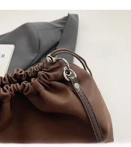 Detail of dark brown matte leather bag with silver metal hooks and drawstring closure