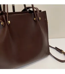 Detail view of smooth dark brown leather tote bag with elegant golden metal hardware accents