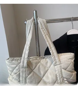 Detail of beige quilted tote bag featuring smooth wide shoulder strap and side zipper pocket