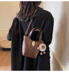 Brown leather bucket bag with gold lock and plush sheep charm on a model's shoulder