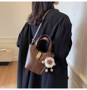 Brown leather bucket bag with gold buckle and plush charm styled on a black coat