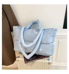 Detail of light blue quilted tote bag with glossy finish on a white suitcase