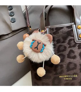 Plush lion bag charm with brown fur and metallic clip on a leopard print bucket bag