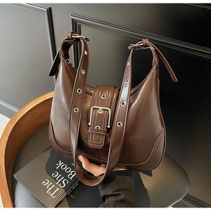 Dettaglio della borsa sottospalla in pelle marrone scuro con occhielli in metallo e fibbia