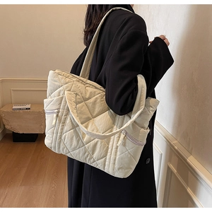 Side view of a large beige quilted tote bag with diamond pattern on a female model