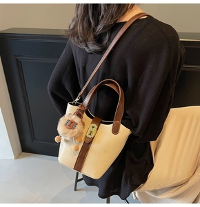 Detail of cream and brown bucket bag featuring a gold metal turn-lock and plush lion charm