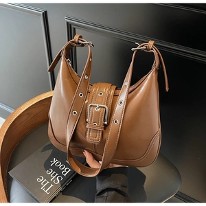 Dettaglio borsa a mezzaluna in pelle marrone con fibbia a cintura e occhielli metallici