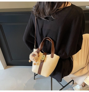 Detail shot of a minimalist cream bucket bag with brown leather trim and plush pendant decoration