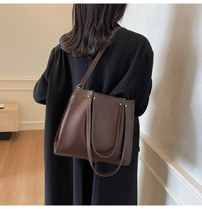Modern brown faux leather tote bag with gold hardware shown on shoulder of a black coat