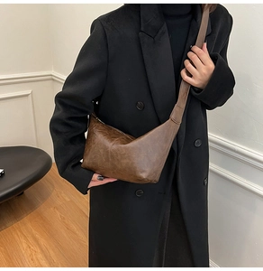 Close-up of a vintage brown half-moon crossbody bag with grainy texture on a black coat