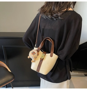 Detail of minimalist cream bucket bag with brown handles and a cute lion charm