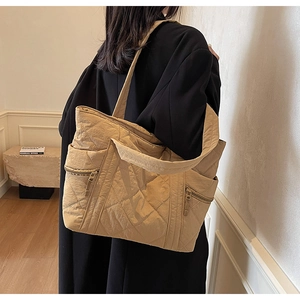 Detailed back view of a khaki quilted tote bag on a black coat with side zipper detail
