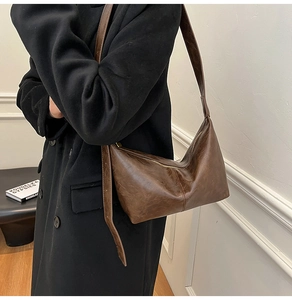Close-up of a dark brown crescent bag showing glossy faux leather texture and zipper