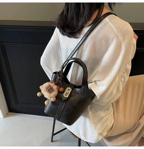 Detail of black leather bucket bag with metal buckle and cute lion plush charm accessory