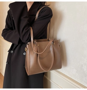 Detailed side view of a large brown tote bag on a model wearing a long black coat