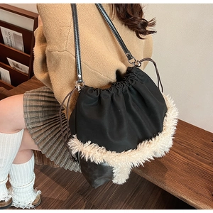 Detail of black drawstring bucket bag with cream faux fur trim worn by a model