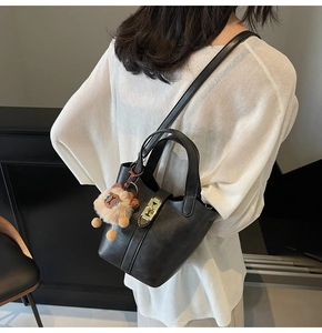 Detailed view of a black leather bucket bag featuring a cute lion plush and gold metal lock