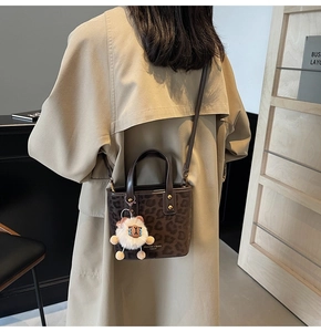 Detail of leopard print bucket bag with plush sheep charm on a beige trench coat
