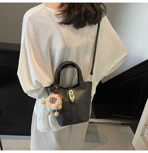 Detail of black leather bucket bag featuring metal lock and cute plush charm on a model