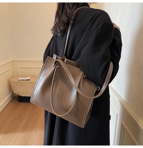 Close-up of brown leather tote bag with fine stitching and dual handles on a model