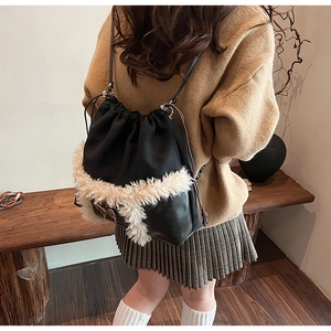 Detail of black drawstring bucket bag featuring white faux shearling trim on base