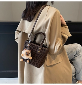 Detailed view of leopard print bucket bag with leather handles and plush lion charm