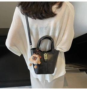 Detail of black leather bucket bag with gold clasp and cute plush lion charm accessory