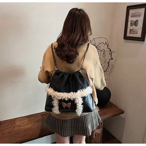 Detail of black drawstring backpack with white faux fur trim and golden butterfly clasp