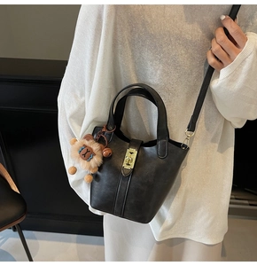 Detail view of black bucket bag with gold lock and cute plush animal charm on model