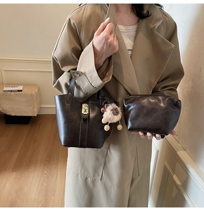 Detail of dark brown bucket bag set with gold lock and sheep plush charm on a beige coat
