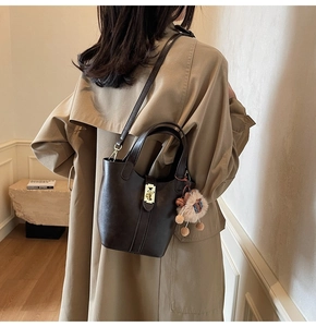 Brown leather bucket bag with gold lock and plush sheep charm shown on a model