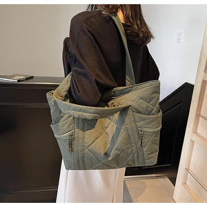 Close-up of olive green quilted tote bag showing side zipper pockets and stitching details